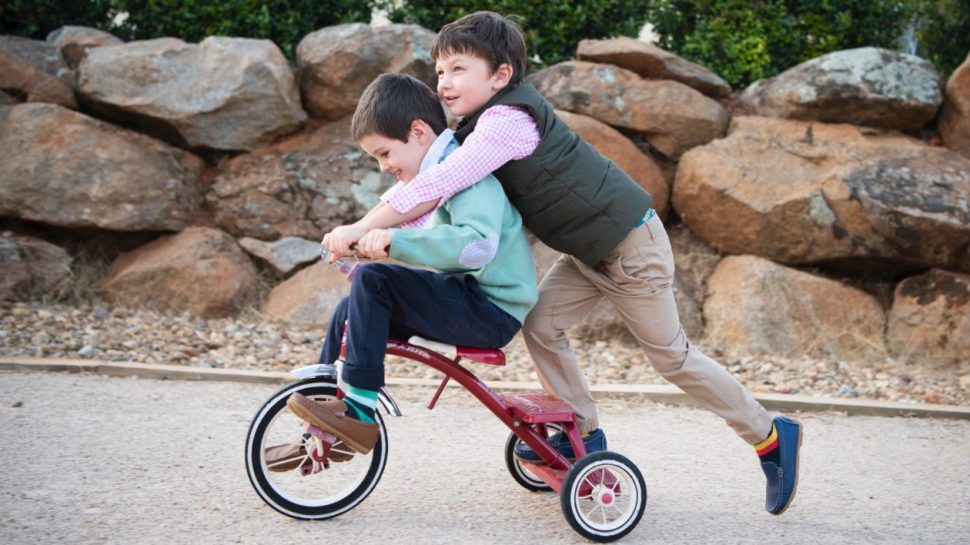 Two small boys playing on a tricycle, wearing Millwoods shoes.