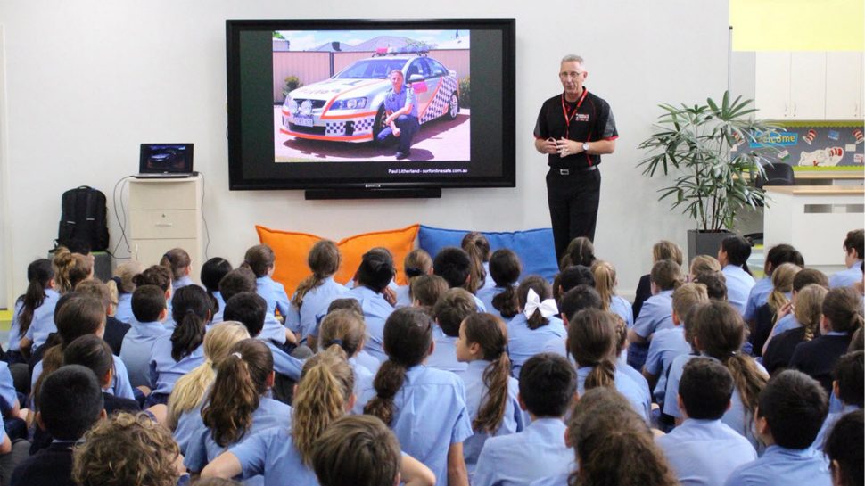 A man delivering a presentation in front of a large group of students at a school 