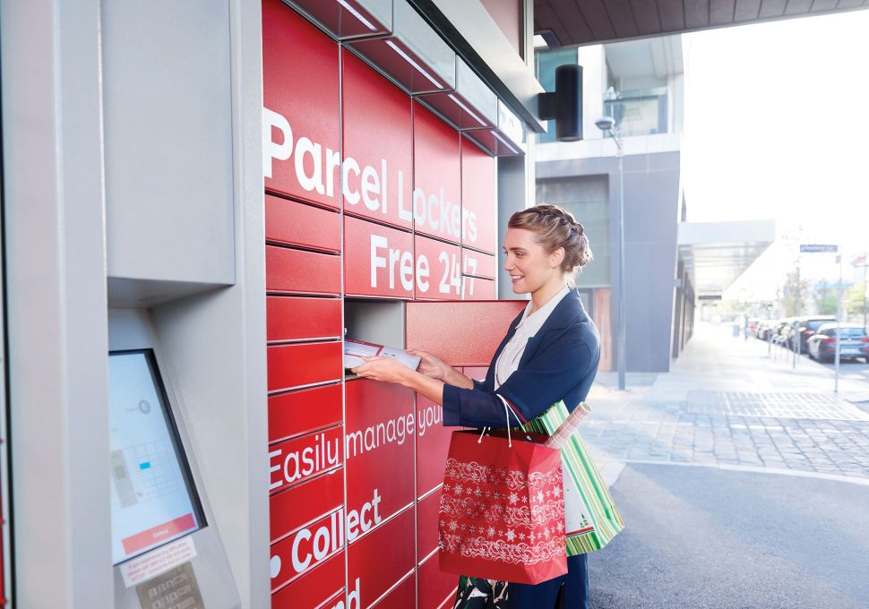 Business woman in blue suit standing at parcel locker, taking a parcel from an open locker