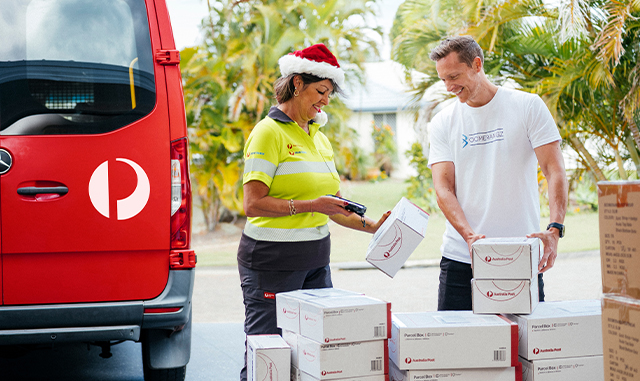 Postie standing outside in front of red Australia Post scanning parcels of small business owner